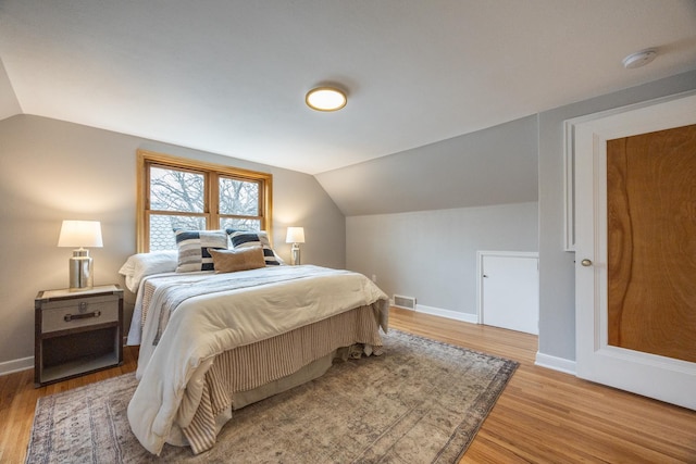 bedroom featuring visible vents, baseboards, lofted ceiling, and light wood-type flooring
