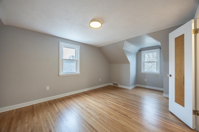 bonus room featuring baseboards, visible vents, vaulted ceiling, and light wood finished floors
