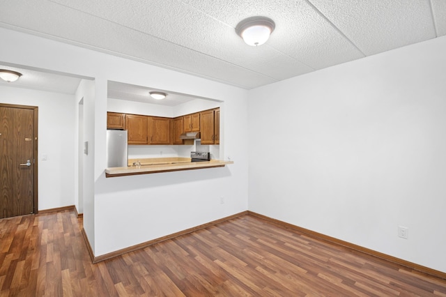 3300 Louisiana Ave S Unit 523, Saint Louis Park, MN 55426 - kitchen featuring under cabinet range hood, light countertops, dark wood-style floors, brown cabinets, and freestanding refrigerator
