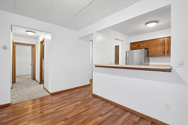 3300 Louisiana Ave S Unit 523, Saint Louis Park, MN 55426 - kitchen featuring freestanding refrigerator, brown cabinets, wood finished floors, a textured ceiling, and a peninsula