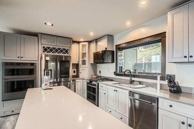 kitchen with glass insert cabinets, recessed lighting, light countertops, a sink, and stainless steel appliances