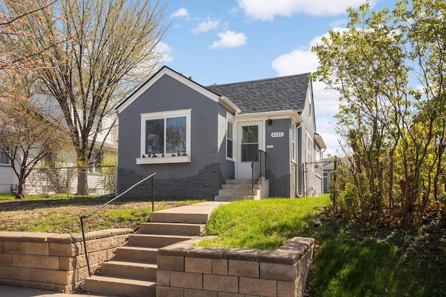 view of front facade with fence, roof with shingles, and stucco siding