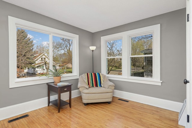 living area featuring visible vents, light wood-style flooring, baseboards, and plenty of natural light