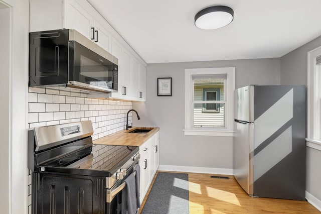 kitchen featuring backsplash, appliances with stainless steel finishes, light wood-type flooring, a sink, and baseboards