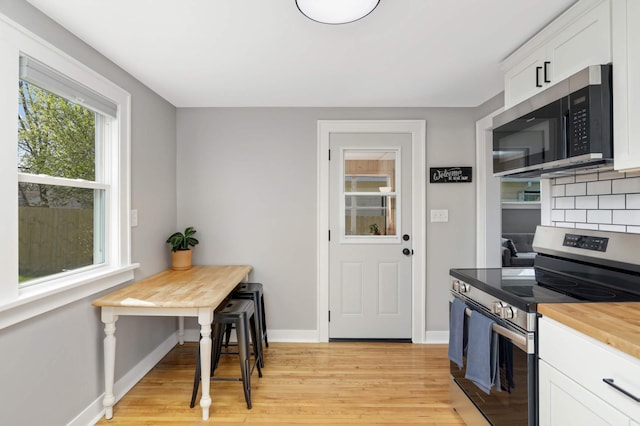 kitchen with butcher block countertops, appliances with stainless steel finishes, baseboards, white cabinets, and light wood-style flooring