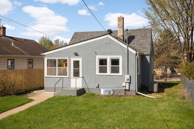 back of house with a chimney, central air condition unit, fence, a yard, and stucco siding