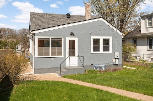 back of house featuring a lawn, fence, a chimney, and a shingled roof