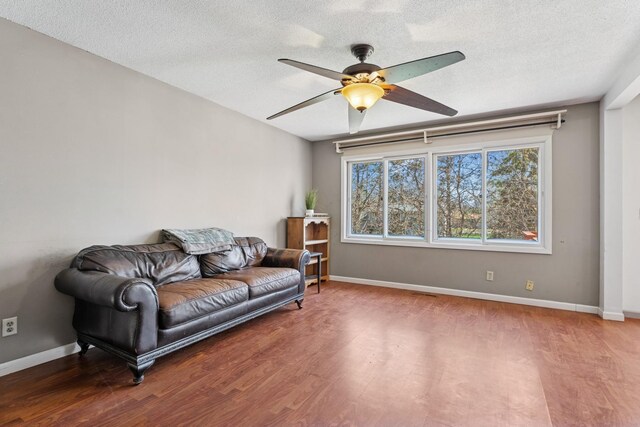 living area with a ceiling fan, baseboards, wood finished floors, and a textured ceiling