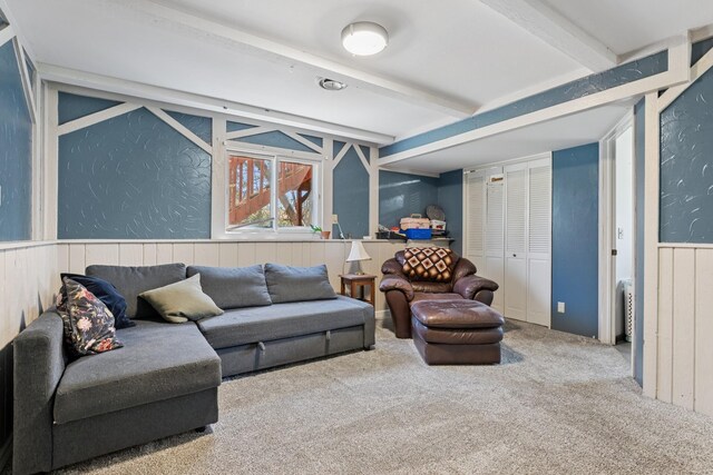 carpeted living room featuring a wainscoted wall and beamed ceiling