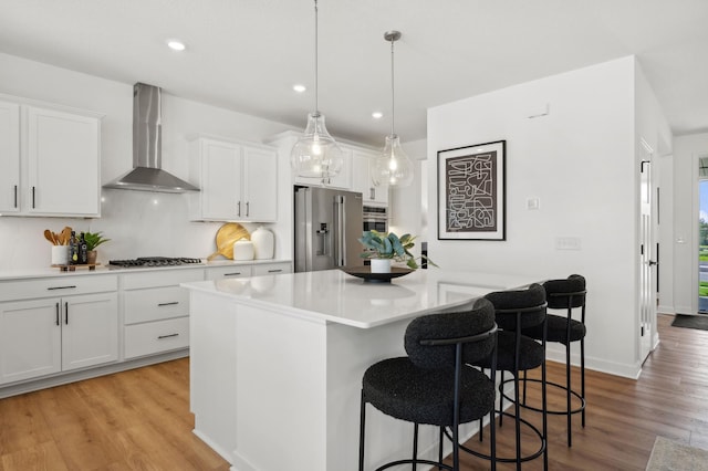 kitchen with a kitchen breakfast bar, wall chimney exhaust hood, white cabinetry, light wood-style flooring, and stainless steel appliances