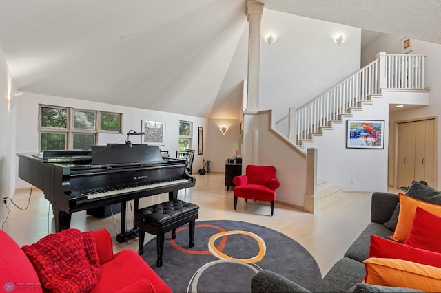 living room with decorative columns, high vaulted ceiling, stairs, and wood finished floors