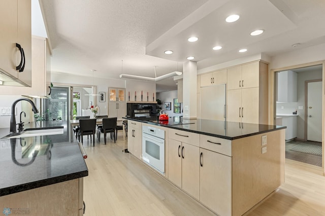 kitchen featuring oven, light wood-type flooring, light brown cabinetry, a kitchen island, and a sink