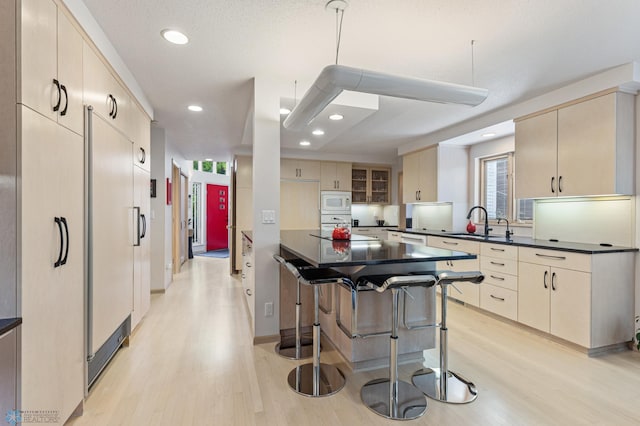 kitchen with light wood-style flooring, a sink, dark countertops, and white microwave