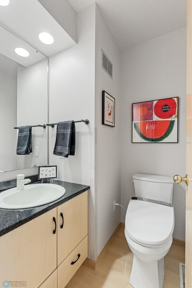 bathroom with visible vents, wood finished floors, toilet, and vanity