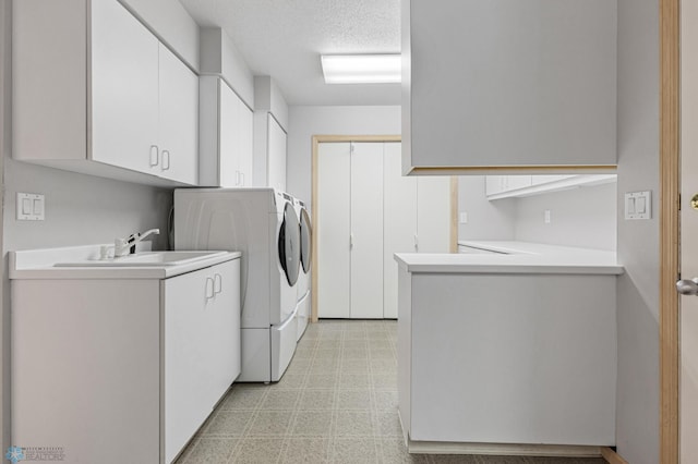laundry area featuring a sink, separate washer and dryer, light floors, a textured ceiling, and cabinet space