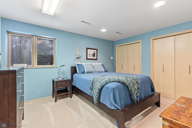 carpeted bedroom with baseboards, visible vents, two closets, and a textured ceiling