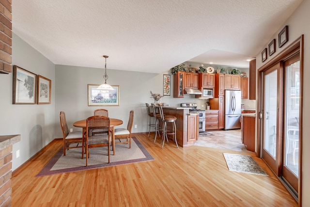 dining space with a textured ceiling, baseboards, and light wood-style flooring