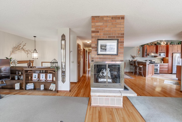 living room with a brick fireplace, a textured ceiling, visible vents, and light wood-type flooring