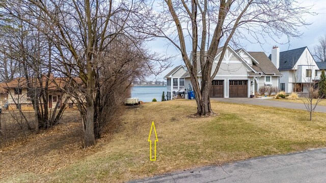 view of front of house with an attached garage, a water view, driveway, and a front yard