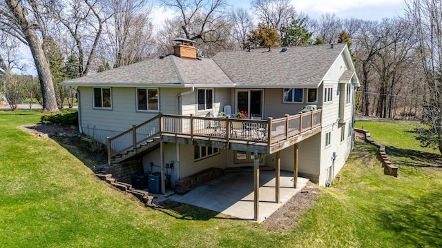 rear view of house with a chimney, roof with shingles, a lawn, a wooden deck, and a patio area
