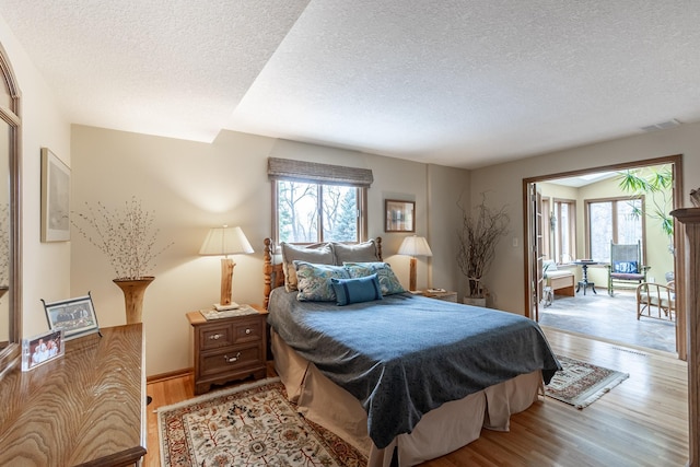 bedroom featuring visible vents, baseboards, a textured ceiling, and wood finished floors