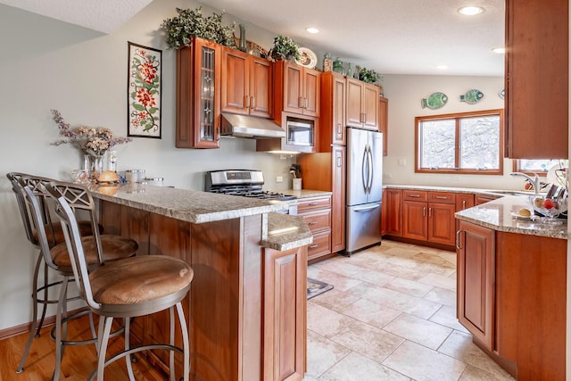 30 Interlachen Ln, Tonka Bay, MN 55331 - kitchen with a peninsula, appliances with stainless steel finishes, glass insert cabinets, a breakfast bar, and brown cabinetry