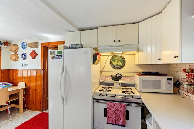 kitchen with under cabinet range hood, white appliances, light countertops, wooden walls, and white cabinetry