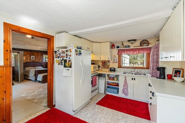 kitchen with white appliances, a sink, light countertops, decorative backsplash, and wood walls