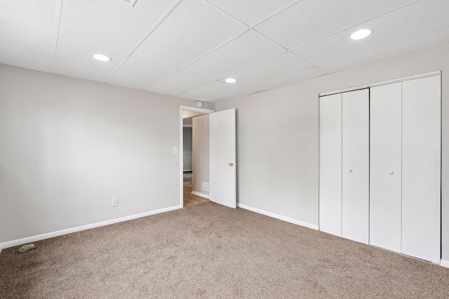 unfurnished bedroom featuring baseboards, a closet, carpet flooring, and a paneled ceiling