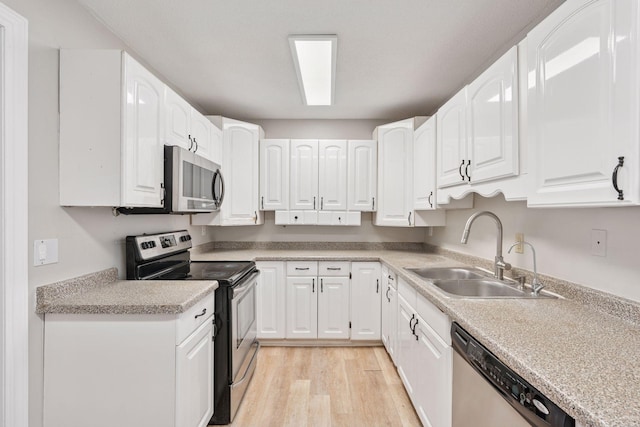 kitchen with a sink, white cabinetry, light wood-style floors, and appliances with stainless steel finishes