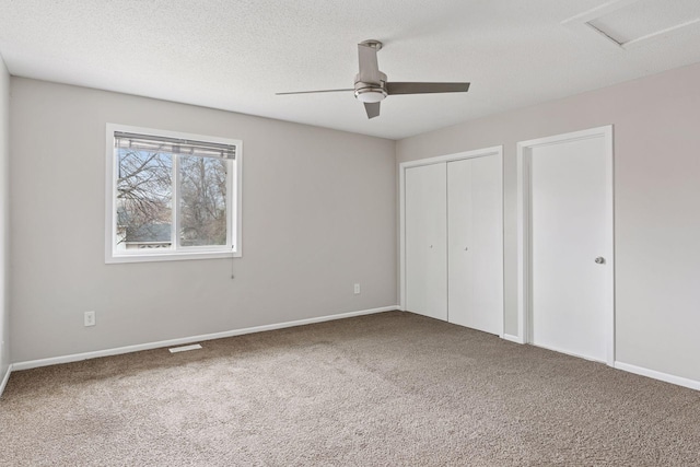 unfurnished bedroom featuring a textured ceiling, carpet, baseboards, ceiling fan, and attic access