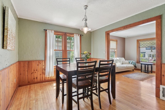 dining room with a textured ceiling, light wood-style flooring, wood walls, a textured wall, and wainscoting