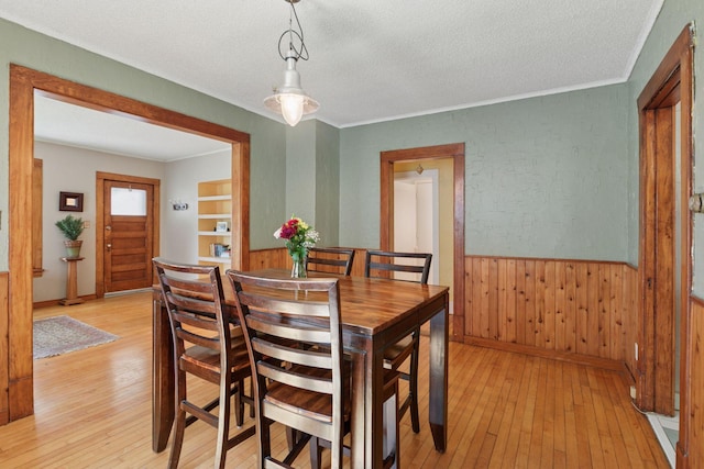 dining space featuring light wood-type flooring, wainscoting, a textured ceiling, and wooden walls