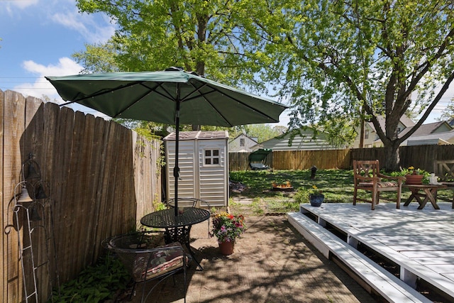 wooden terrace with a storage unit, an outbuilding, and a fenced backyard
