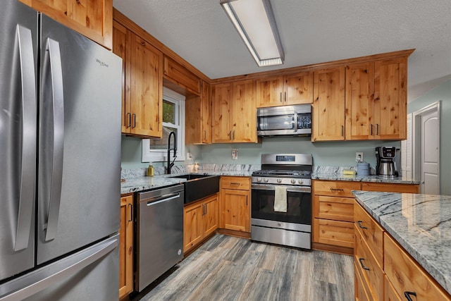 257 Elm Dr, Foley, MN 56329 - kitchen featuring stainless steel appliances, light wood-type flooring, light stone countertops, and a textured ceiling
