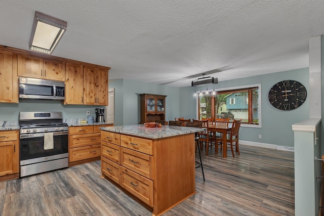 257 Elm Dr, Foley, MN 56329 - kitchen with stainless steel appliances, dark wood-style floors, a kitchen breakfast bar, light stone counters, and a center island