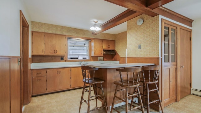kitchen featuring a kitchen bar, light countertops, a peninsula, light floors, and under cabinet range hood