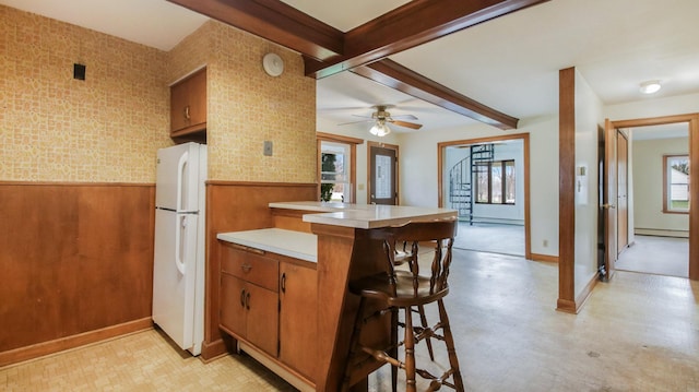 kitchen featuring beam ceiling, light countertops, brown cabinetry, a wainscoted wall, and freestanding refrigerator