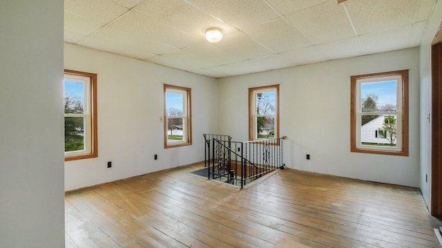 empty room featuring a drop ceiling, a wealth of natural light, and hardwood / wood-style floors