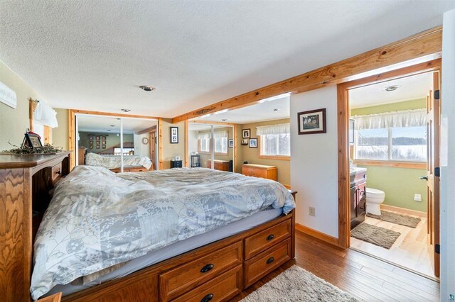 4463 Singkoffer Rd, Summit Twp, WI 54880 - bedroom with wood finished floors, a textured ceiling, baseboards, multiple windows, and connected bathroom