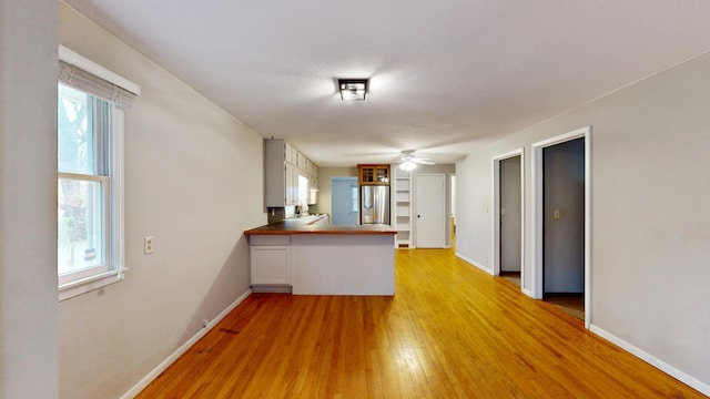 unfurnished living room with ceiling fan, light wood-type flooring, and baseboards