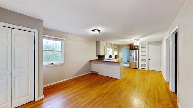 kitchen with ceiling fan, a peninsula, stainless steel fridge, and light wood-style floors