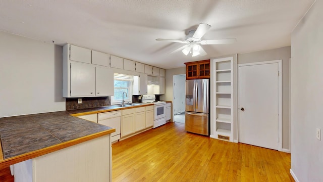 kitchen with a sink, light wood-type flooring, a ceiling fan, a peninsula, and white appliances