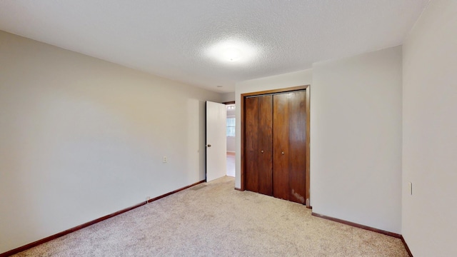 unfurnished bedroom featuring carpet flooring, baseboards, a textured ceiling, and a closet