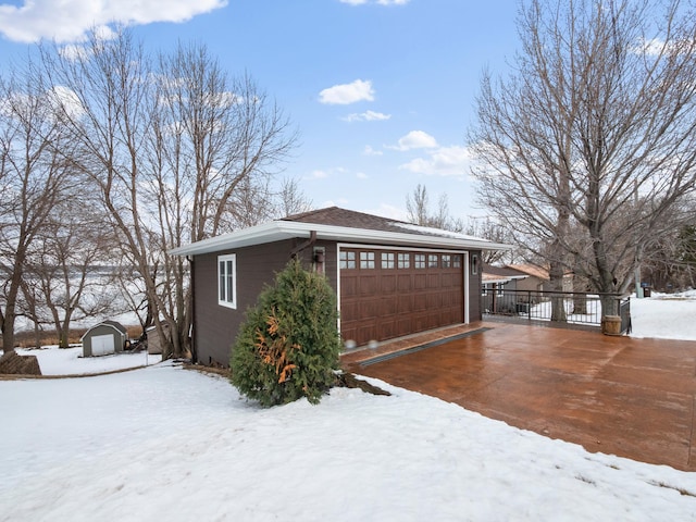 view of snow covered exterior with an outbuilding, a storage unit, a garage, and fence