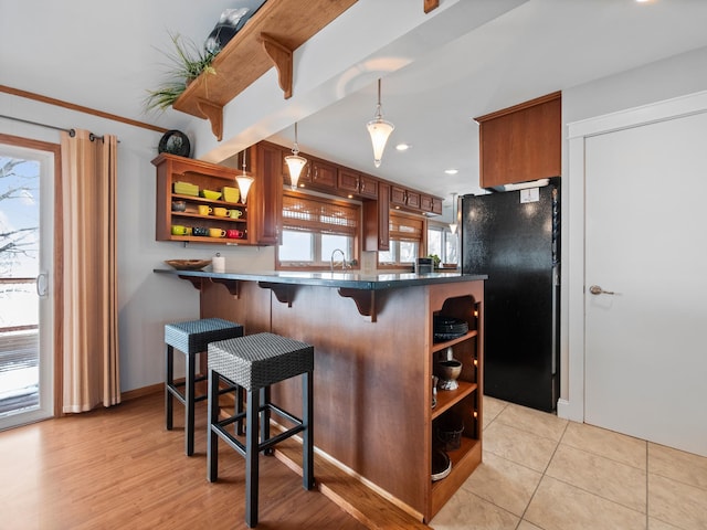 kitchen featuring open shelves, a sink, freestanding refrigerator, a breakfast bar, and a peninsula