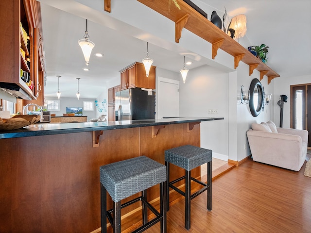 kitchen featuring stainless steel refrigerator with ice dispenser, open floor plan, dark countertops, light wood-style floors, and brown cabinets