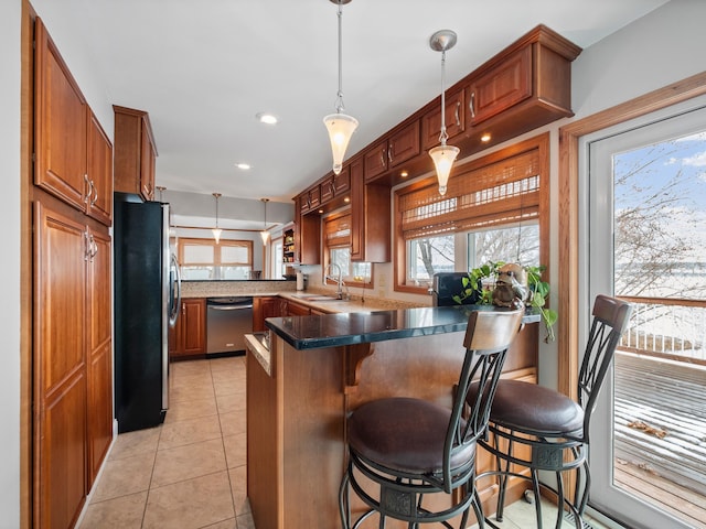 kitchen featuring a breakfast bar, a peninsula, appliances with stainless steel finishes, a sink, and hanging light fixtures