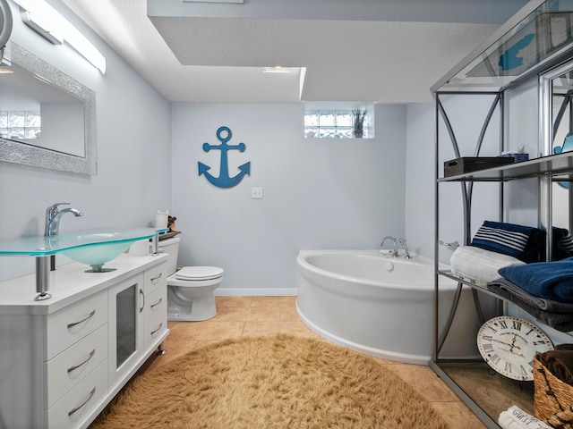 bathroom with a bathing tub, vanity, toilet, tile patterned floors, and baseboards