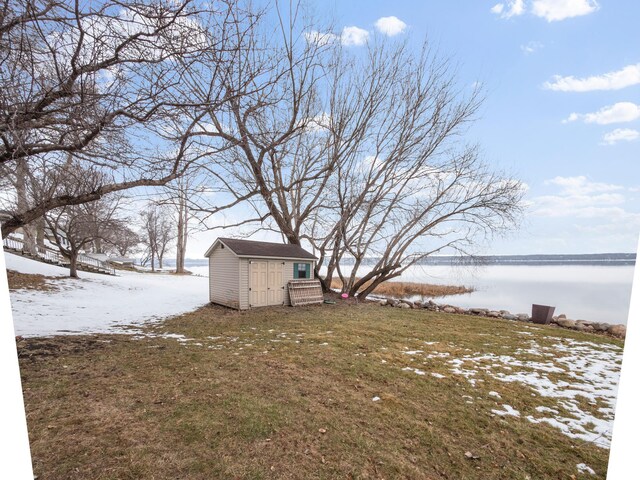 yard covered in snow featuring an outbuilding, a storage shed, and a water view